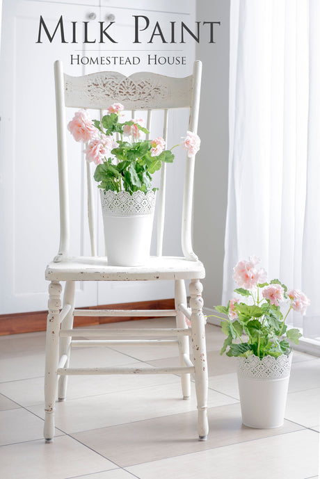 White vintage chair in Homestead House Limestone Milk Paint holding a pink flower pot; text reads “Milk Paint.”.
