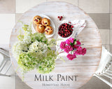 Round table displaying muffins, cherries, flowers, and Homestead House Limestone Milk Paint text on the tabletop.