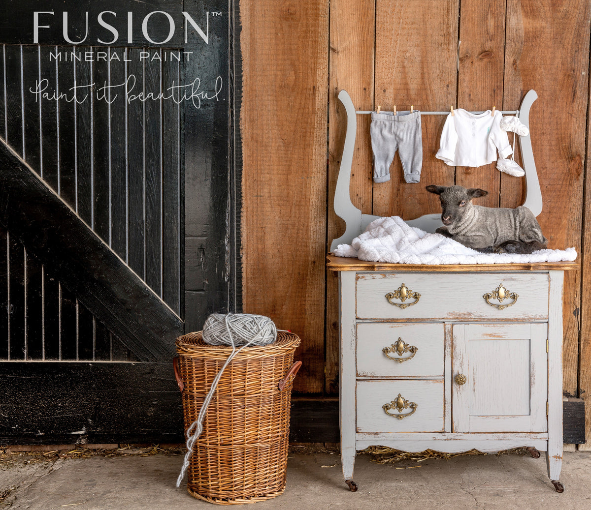 Small dresser painted in Little Lamb by Fusion, with baby clothes inside and a wicker basket of yarn nearby.