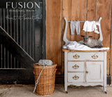 Small dresser painted in Little Lamb by Fusion, with baby clothes inside and a wicker basket of yarn nearby.