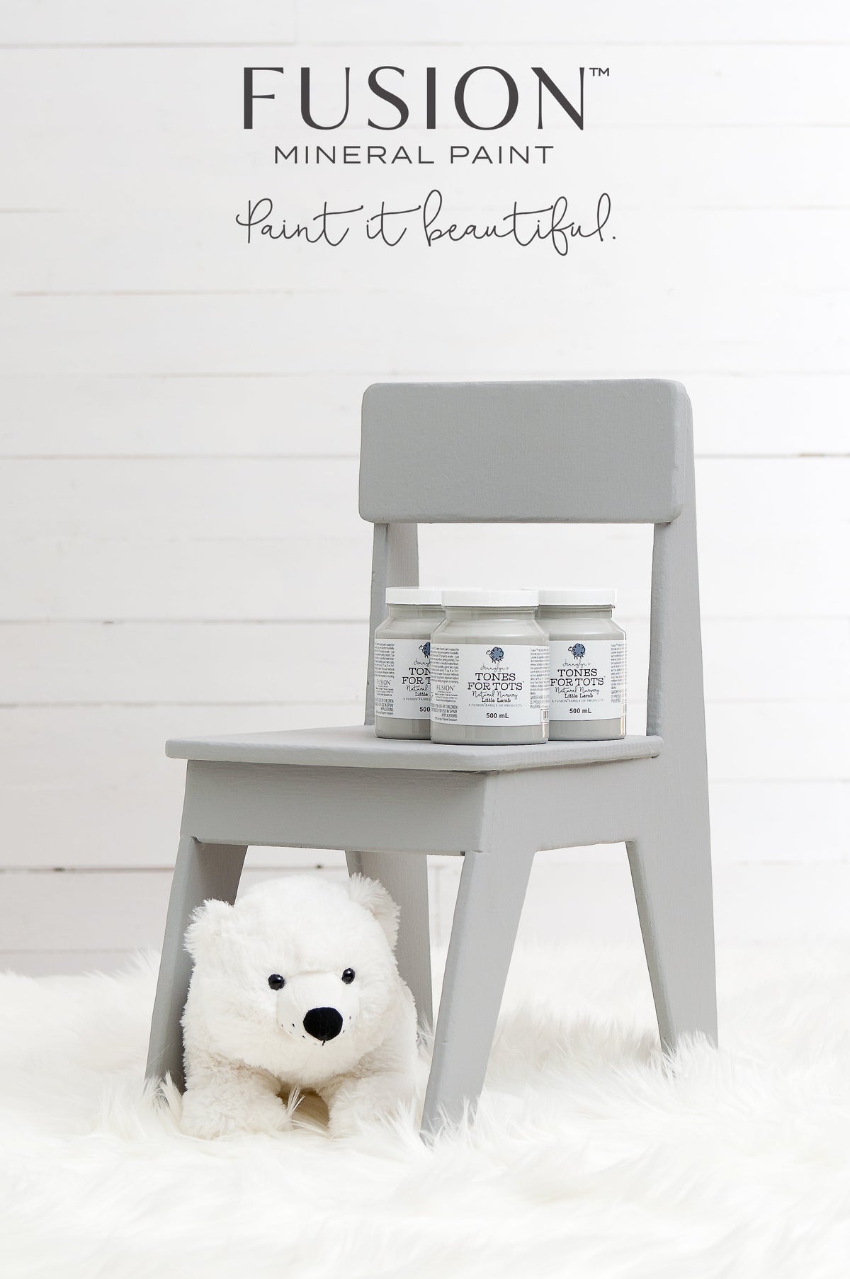 Little Lamb Fusion Mineral Paint jars on a small gray chair; plush bear on white rug below.