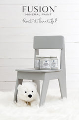 Little Lamb Fusion Mineral Paint jars on a small gray chair; plush bear on white rug below.