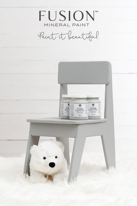 Little Lamb Fusion Mineral Paint jars on a small gray chair; plush bear on white rug below.