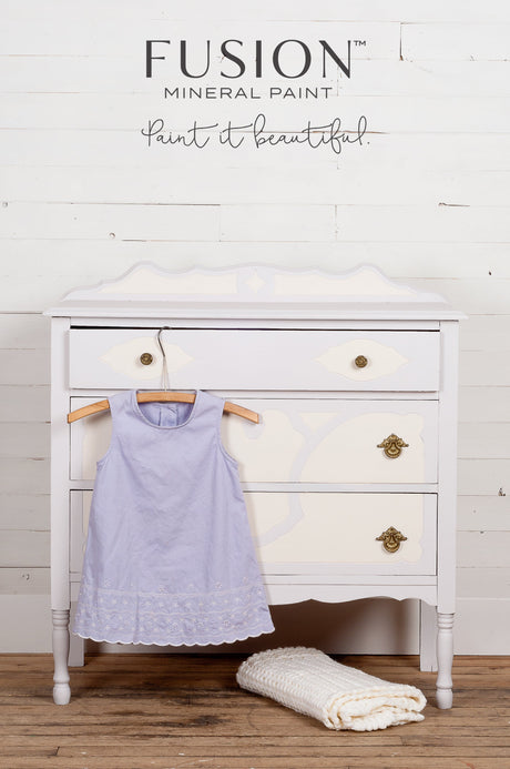 White vintage dresser with gold handles, painted in Fusion’s Little Stork, shown with lavender dress and blanket.