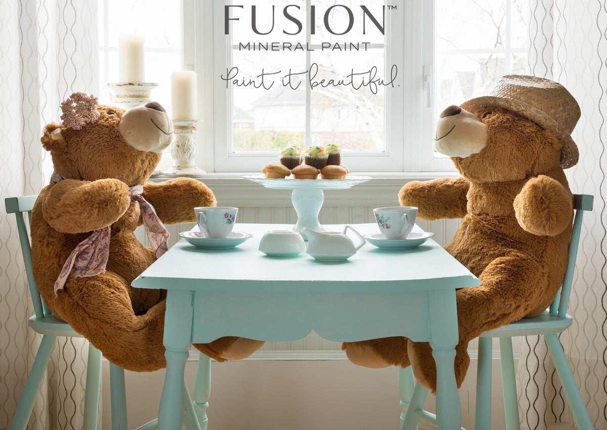 Two teddy bears at a Little Teapot Fusion Mineral Paint table with tea and pastries.