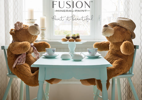 Two teddy bears at a Little Teapot Fusion Mineral Paint table with tea and pastries.