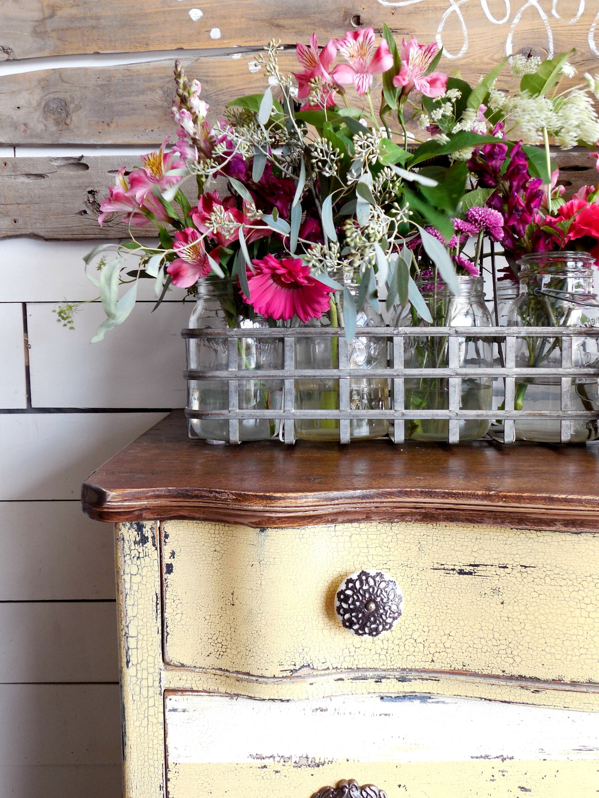Distressed yellow dresser painted with Love Bug by Old Fashioned Milk Paint, topped with glass jars of flowers.