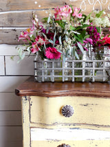 Distressed yellow dresser painted with Love Bug by Old Fashioned Milk Paint, topped with glass jars of flowers.