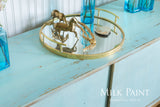 Brass tray with horse figurines and shell on Homestead House Loyalist Milk Paint cabinet, blue bottles nearby.