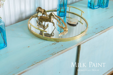 Brass tray with horse figurines and shell on Homestead House Loyalist Milk Paint cabinet, blue bottles nearby.