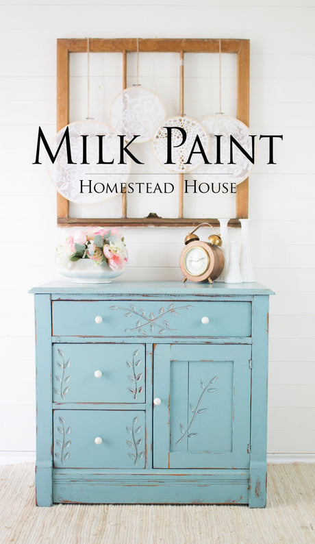 Blue cabinet with floral carvings, white knobs, and “Loyalist Milk Paint by Homestead House” above the clock.