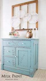 Blue distressed cabinet finished in Homestead House Loyalist Milk Paint, displayed beneath a window.