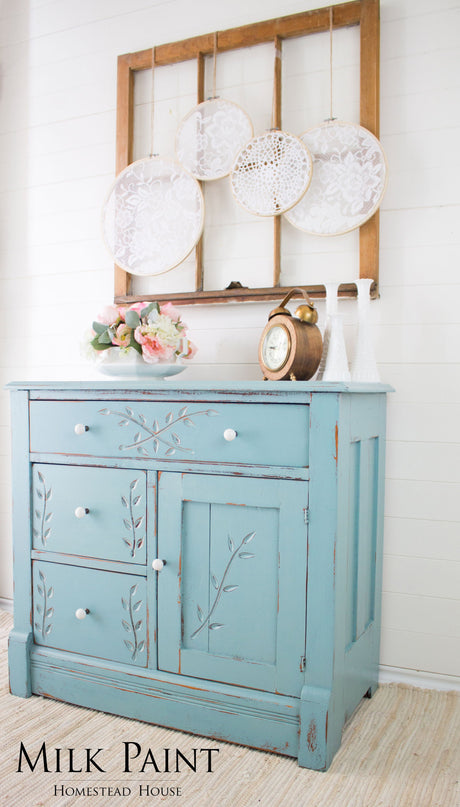 Blue distressed cabinet finished in Homestead House Loyalist Milk Paint, displayed beneath a window.
