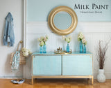 Light blue cabinet with white vases, round gold mirror, and wall painted in Loyalist Milk Paint by Homestead House.