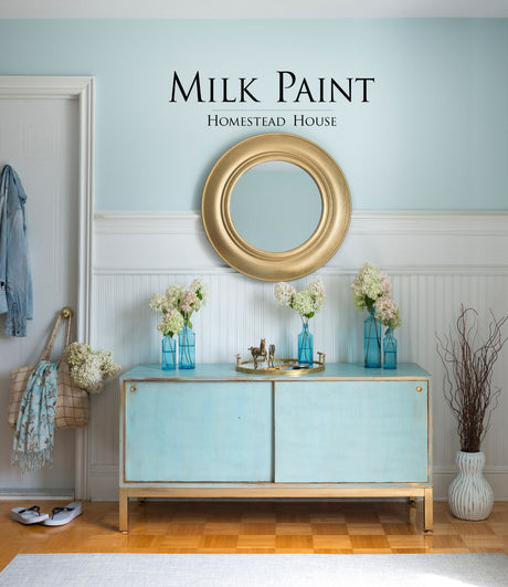 Blue cabinet with gold trim, topped with a gold mirror and flowers; “Loyalist Milk Paint by Homestead House” on wall.