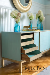 Blue sideboard painted with Homestead House Loyalist Milk Paint, open drawers, hydrangeas, gold horse, round mirror.