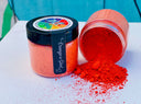 Two jars of DIY Paint Co. Making Powder, one tipped and spilling vibrant orange powder on a white surface.