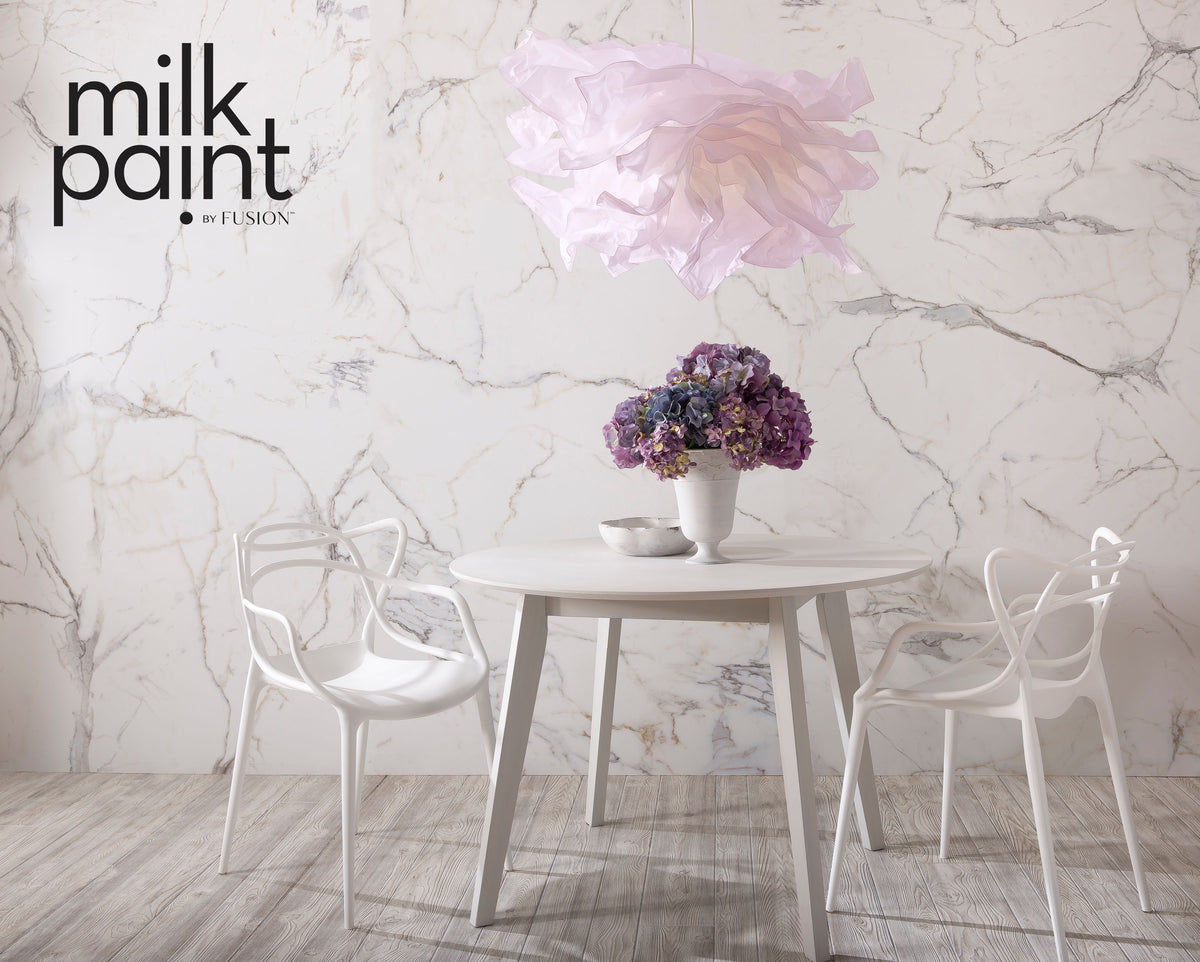 Round white table with two chairs and a vase under a pink pendant against a Marble Milk Paint wall by Fusion Mineral Paint.