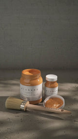 Three jars of Marigold Alchemy Paint by Fusion Mineral Paint with brush and paint sample on gray surface.