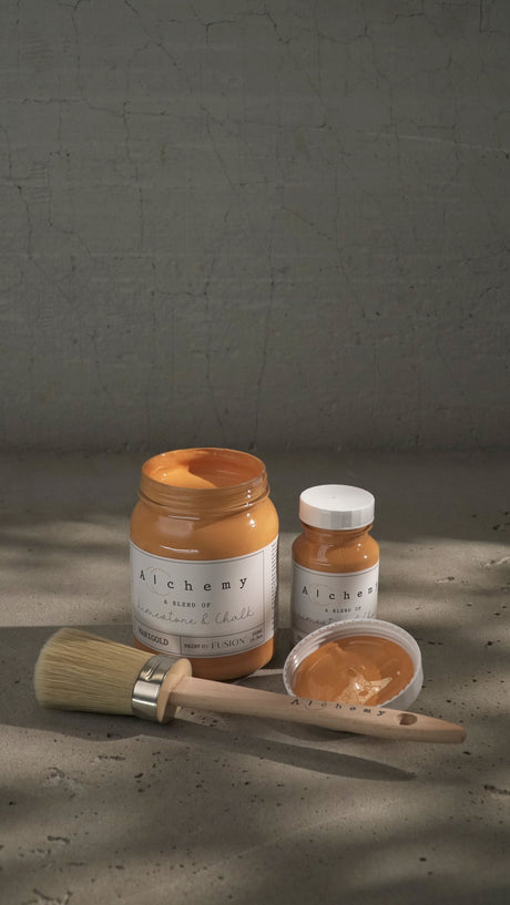 Three jars of Marigold Alchemy Paint by Fusion Mineral Paint with brush and paint sample on gray surface.