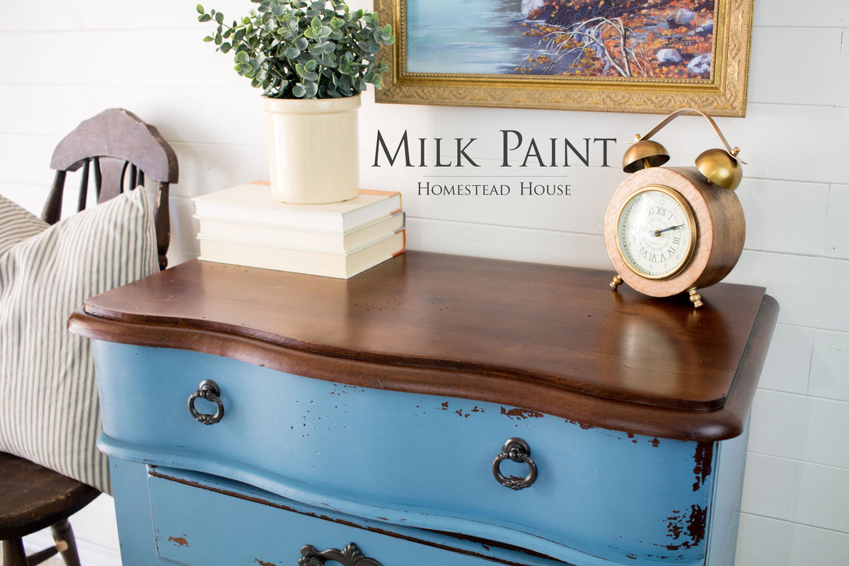 Blue distressed dresser in Homestead House Maritime Blue Milk Paint with wood top; books and a plant on top.