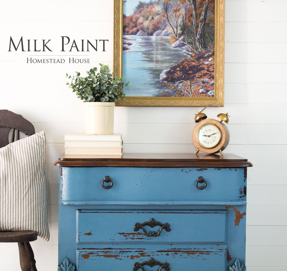 Blue dresser in Homestead House Maritime Blue Milk Paint with vintage clock, plant, and river art on shiplap wall.