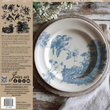 Round plate with blue bird motif on a mat, beside a napkin and Meadowlark Stamp by IOD instructions.