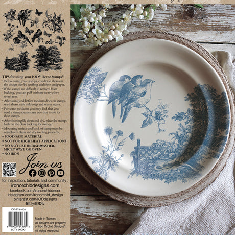 Round plate with blue bird motif on a mat, beside a napkin and Meadowlark Stamp by IOD instructions.