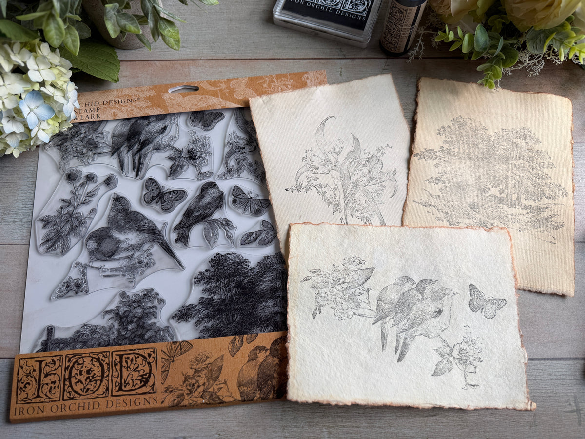 I.O.D. Meadowlark Stamp set with clear bird and butterfly stamps, ink pads, and textured paper on floral wood surface.