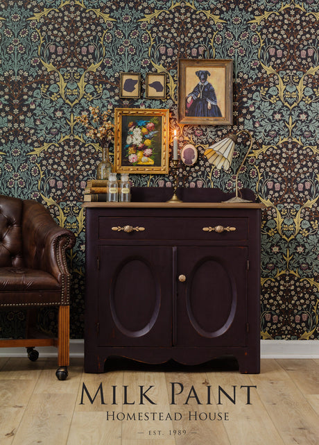 Dark wood cabinet with vintage decor and leather chair, featuring Mennonite Red by Homestead House against floral wallpaper.
