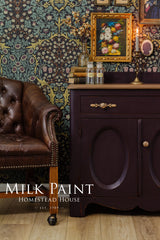 Homestead House Mennonite Red Milk Paint cabinet with brown leather chair, floral wallpaper, and art in background.