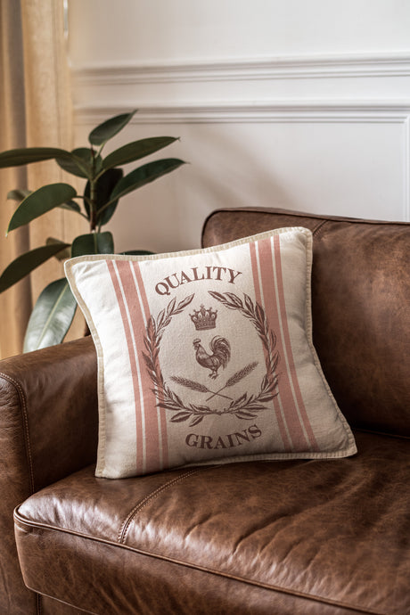 Cream pillow with Mercantile Stamp by IOD on leather couch next to green plant.