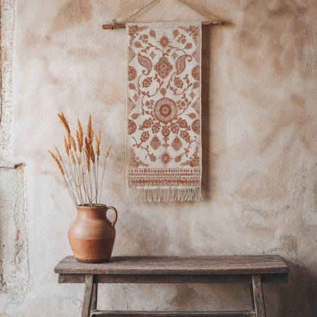 Clay vase with dried grass sits on a bench, beneath tapestry featuring an I.O.D. Mercy House Chitenge Stamp.