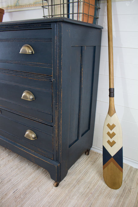 Wooden dresser with three drawers painted Homestead House Midnight Blue Milk Paint, shown on a striped rug.
