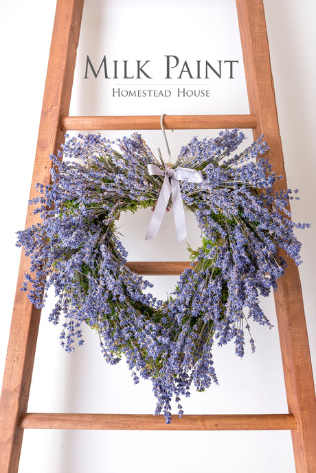Heart-shaped lavender wreath with silver bow displayed on a ladder.