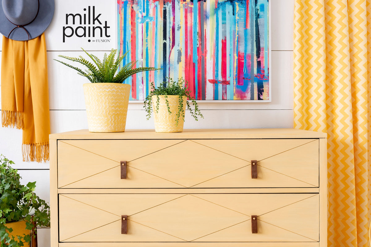 Yellow dresser painted with Fusion Mod Mustard Milk Paint, shown near plants, art, and yellow curtains.