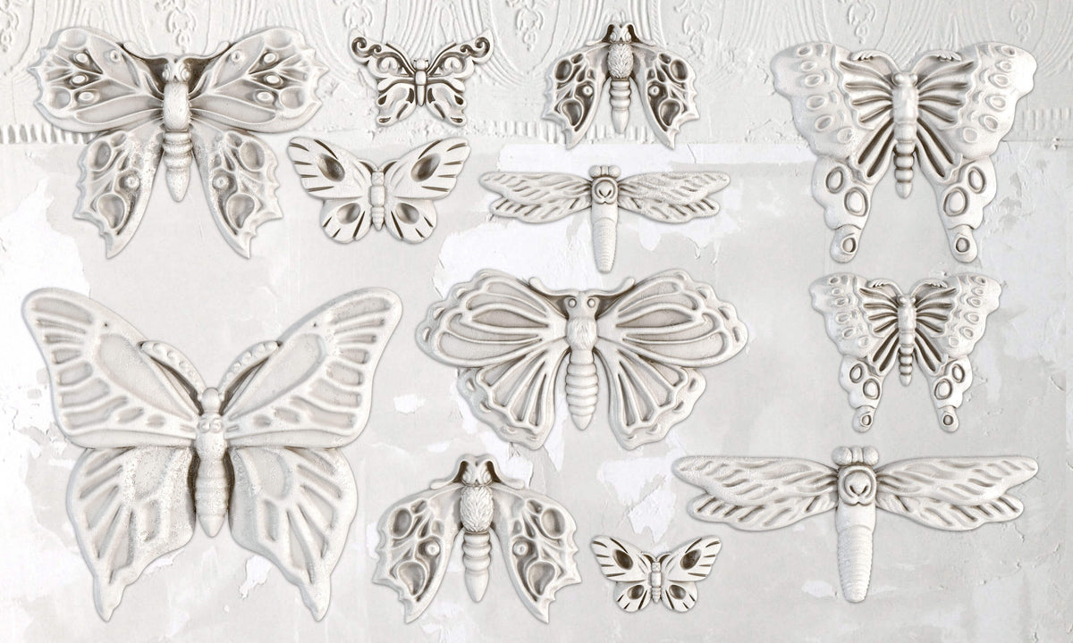 Twelve white I.O.D. Monarch Mould ornaments displayed on a textured off-white wall with a patterned border.
