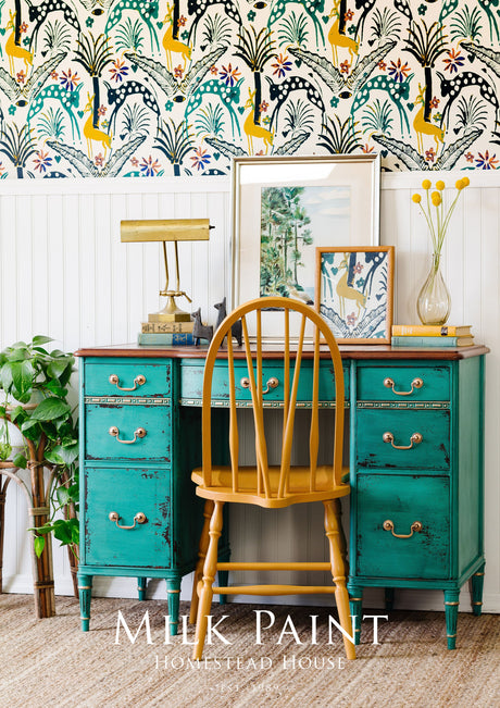 Teal vintage desk finished with Homestead House Montclair Milk Paint placed in front of colorful wallpaper.