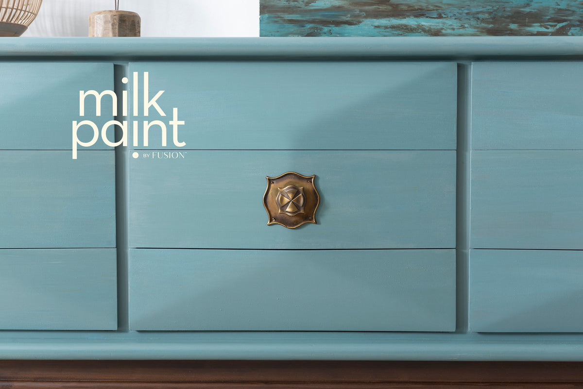 Blue dresser with brass handle; “Monterey Milk Paint by Fusion Mineral Paint” text displayed on the left.