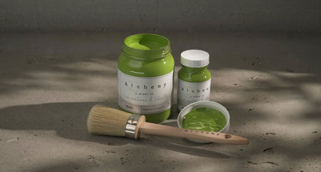 Three Moss Alchemy Paint containers by Fusion Mineral Paint with a paintbrush on a gray surface.