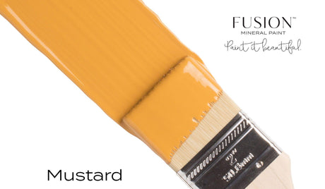 Paintbrush dipped in Mustard Fusion Mineral Paint, all-in-one acrylic by Fusion Mineral Paint.