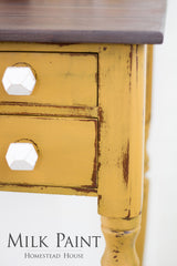 Distressed yellow table with two drawers, white knobs, and Mustard Milk Paint by Homestead House label.
