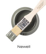 Flat brush with sage green paint rests on open jar; “Newell Fusion Mineral Paint” text visible below.