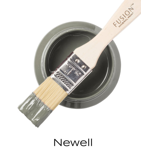 Flat brush with sage green paint rests on open jar; “Newell Fusion Mineral Paint” text visible below.
