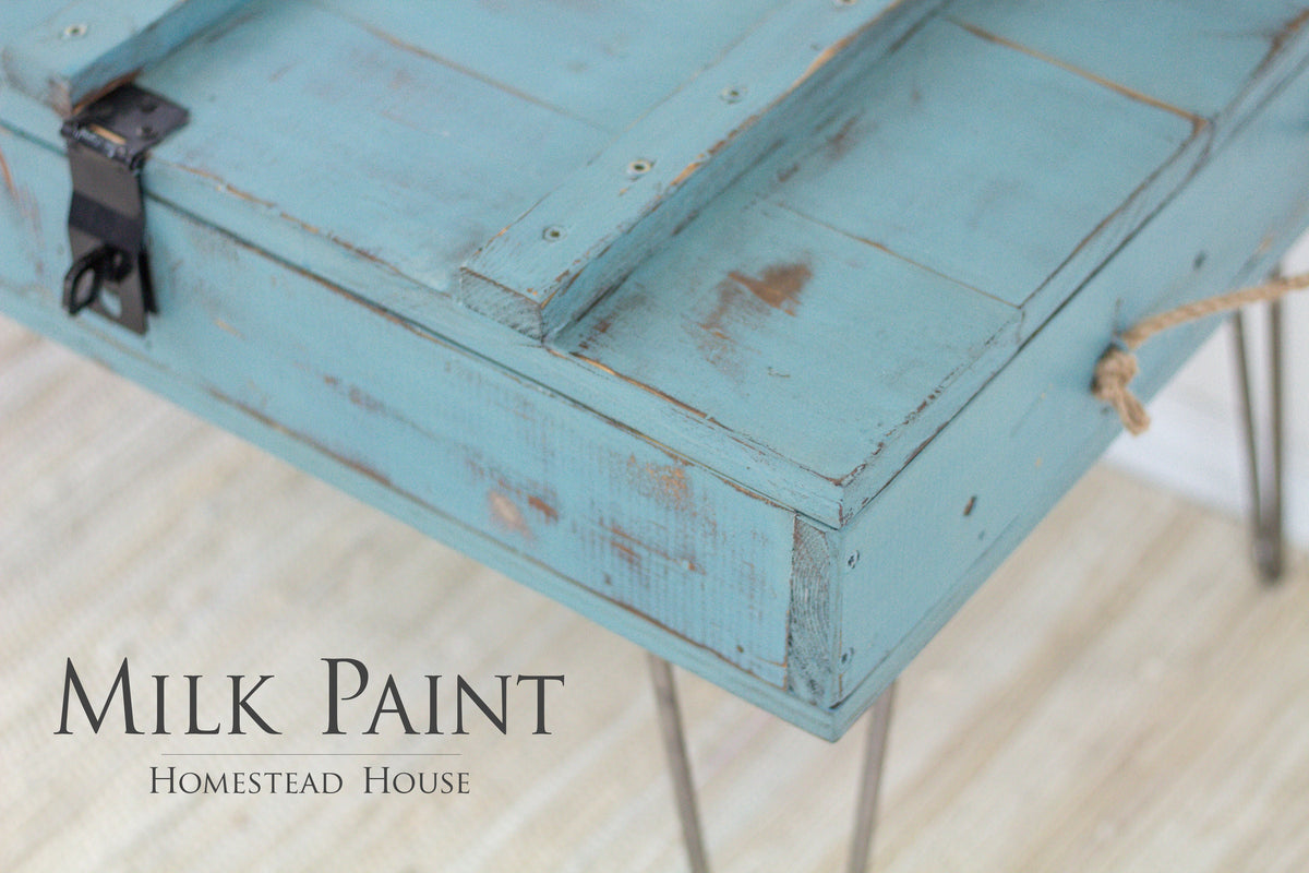Distressed green wooden box on metal legs, labeled “Niagara Green Milk Paint by Homestead House.”.