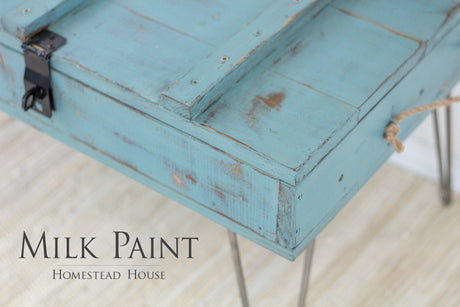 Distressed green wooden box on metal legs, labeled “Niagara Green Milk Paint by Homestead House.”.