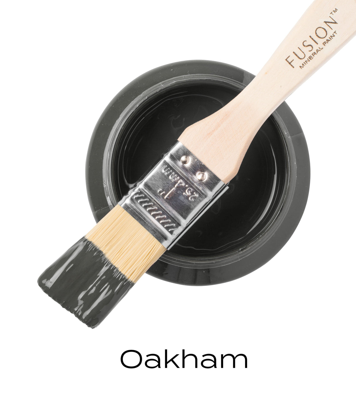 Brush with dark gray Oakham Fusion Mineral Paint on open jar labeled “Oakham” in black text.