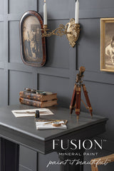 Vintage desk with books, telescope, and sconce against a matte gray Oakham Fusion Mineral Paint wall.
