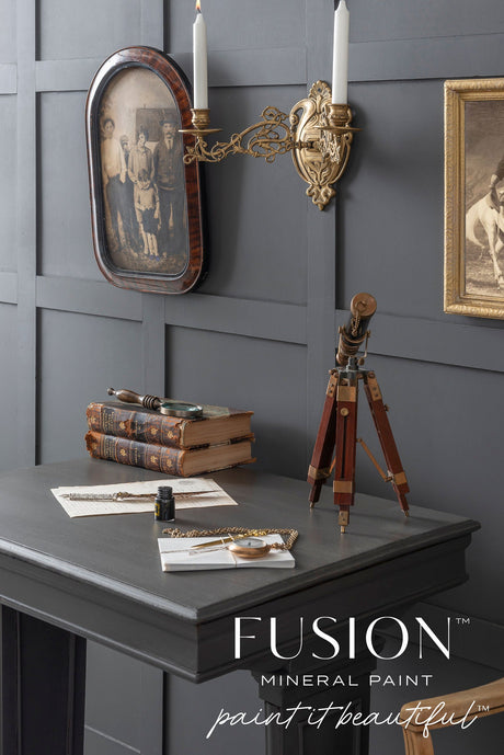 Vintage desk with books, telescope, and sconce against a matte gray Oakham Fusion Mineral Paint wall.