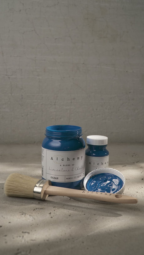Paintbrush with two jars of Fusion Mineral Paint, Ocean Alchemy color, displayed on a gray surface.